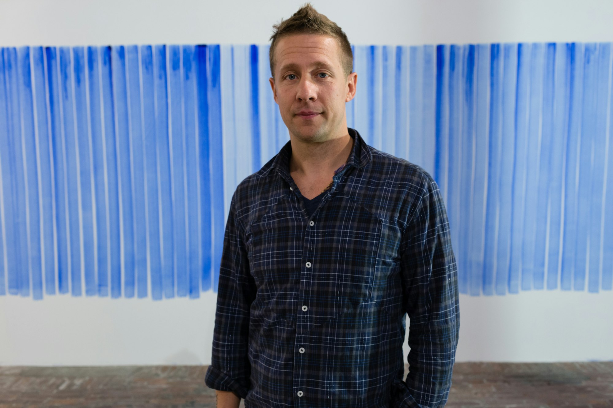 Kunsteneren Jeppe Hein foran en hvit vegg med blå penselstrøk på.