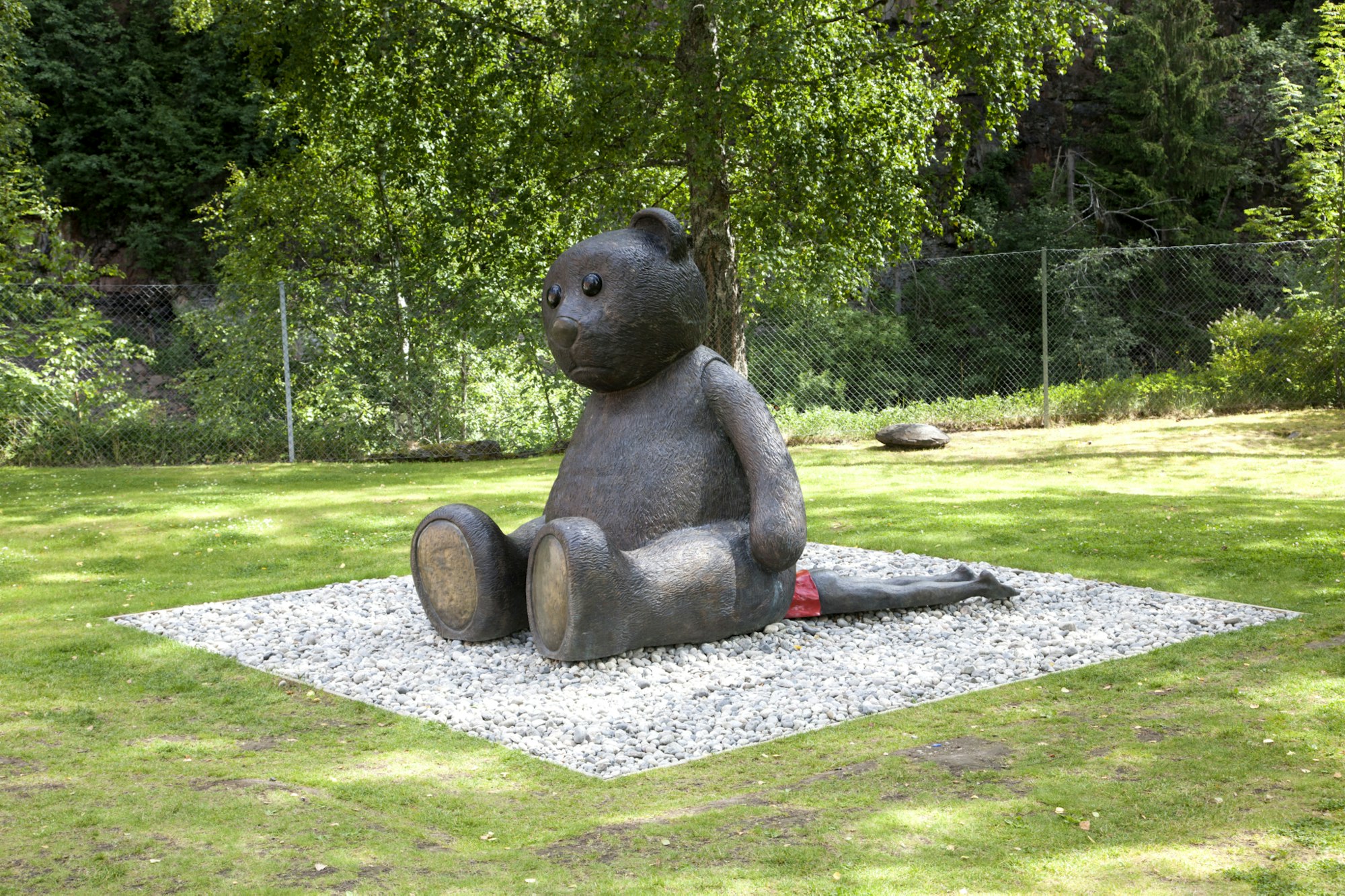 Skulptur, teddybjørn i bronse. Sitter på et menneske.