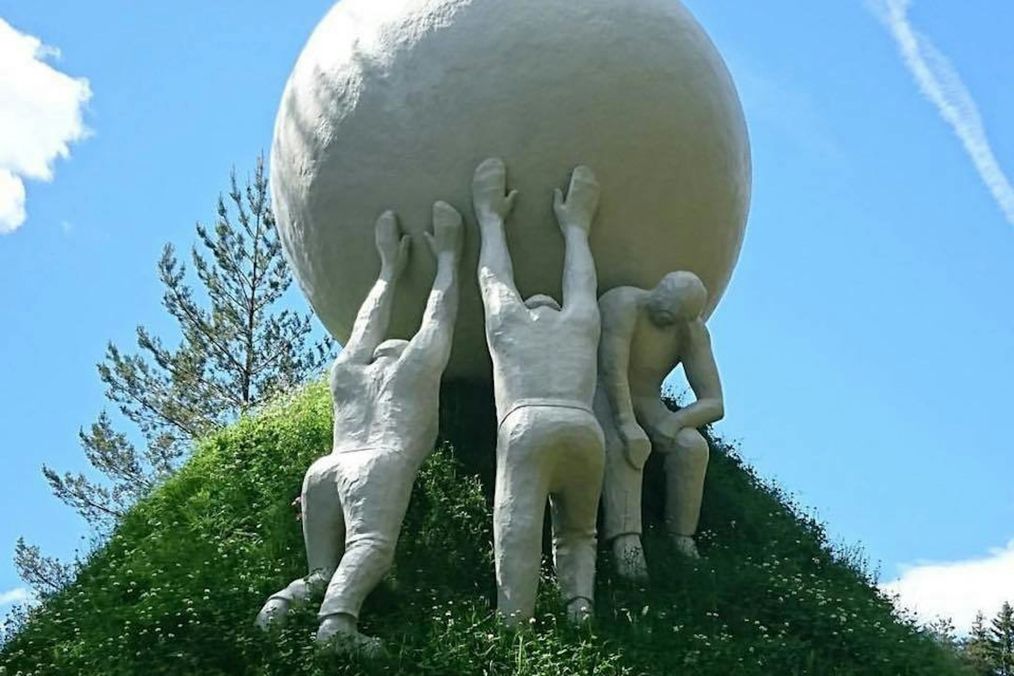 Sculpture, three men pushing a giant ball up a hill.