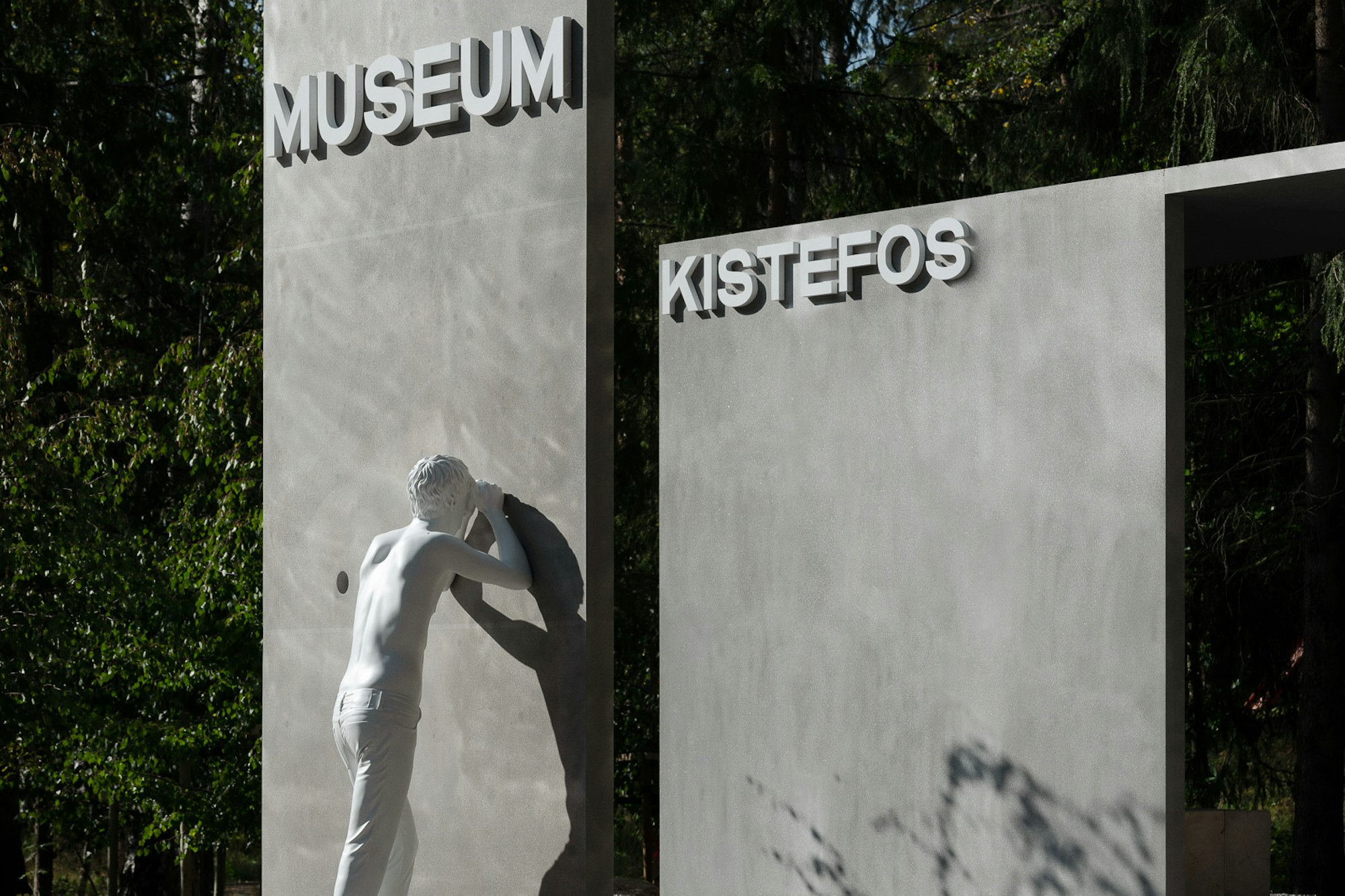 Skulpturen viser en hvit mann som kikker gjennom et hull i veggen på inngangspartiet til Kistefos.