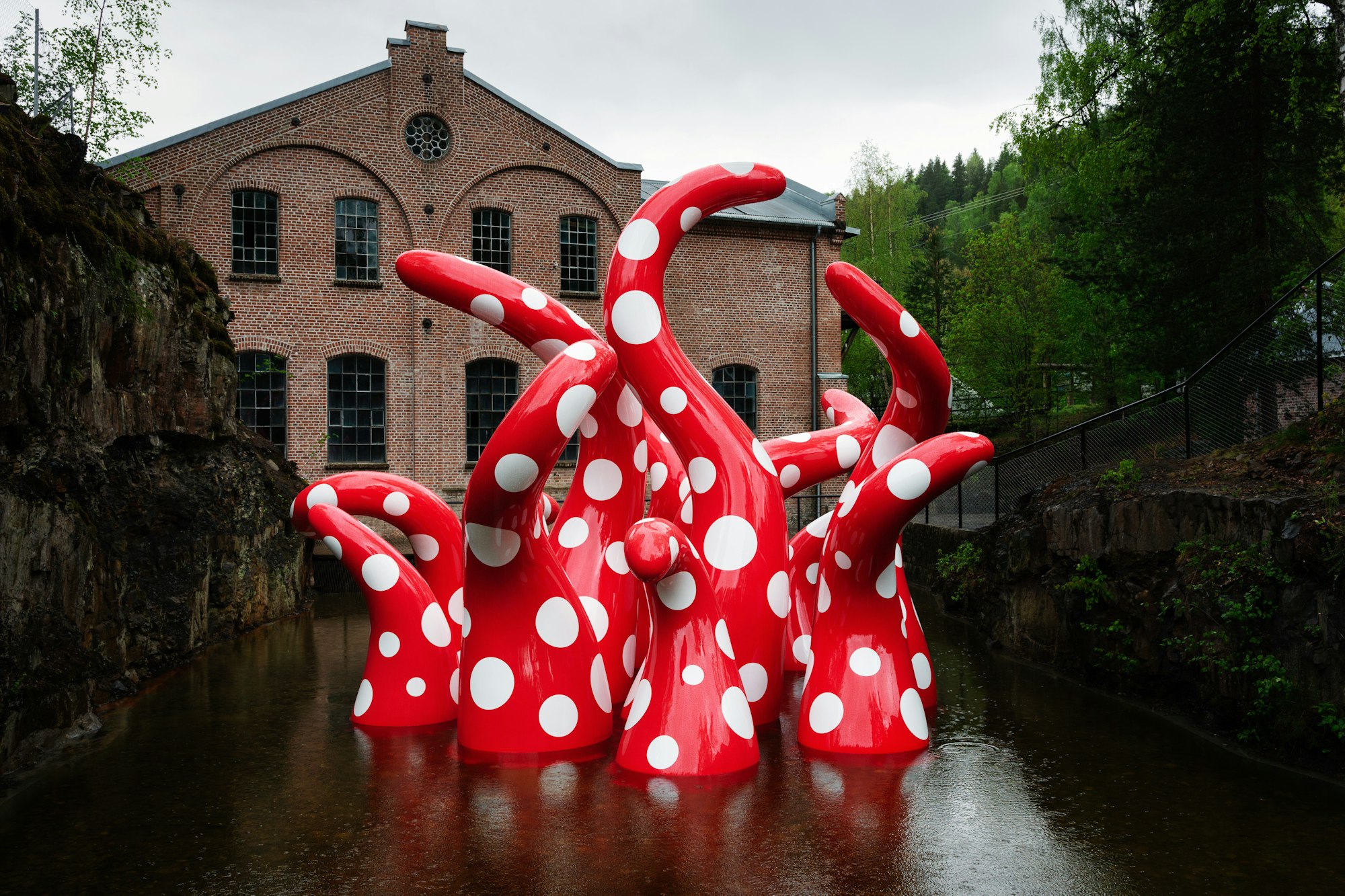 Sculpture by japaneese artist Yayoi Kusama showing octopuslike red and white dotty arms emerging up from the water.